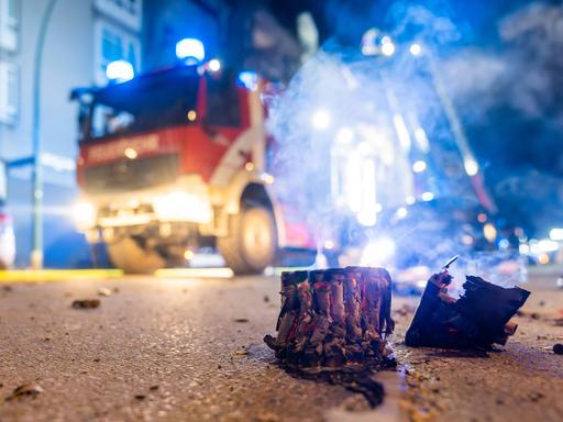 Abgebrannte Böller liegen auf einer Straße in Berlin, im Hintergrund steht ein Feuerwehrauto.