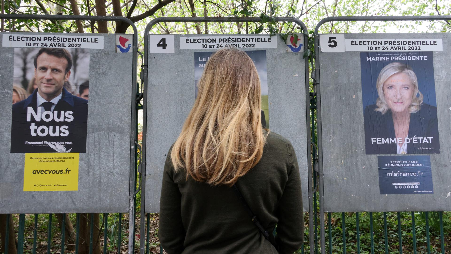 Eine junge Frau steht vor Wahlplakaten von Emmanuel Macron und Marine Le Pen in der Rue de Babylone in Paris, April 2022. Eine junge Frau steht vor Wahlplakaten von Emmanuel Macron und Marine Le Pen in der Rue de Babylone in Paris, April 2022.