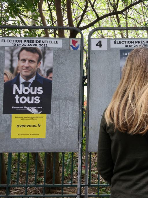 Eine junge Frau steht vor Wahlplakaten von Emmanuel Macron und Marine Le Pen in der Rue de Babylone in Paris, April 2022.