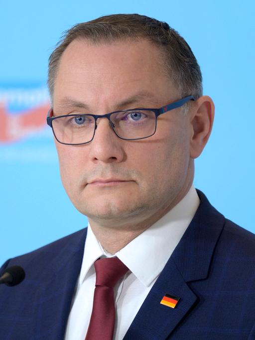 Tino Chrupalla , Co-Vorsitzender der AfD-Fraktion im Bundestag , im Porträt vor einer hellblauen Wand mit AfD-Logo