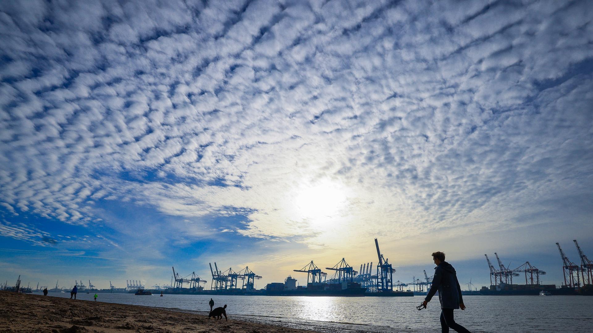 Spaziergänger sind am Strand von Ãvelgönne an der Elbe vor der Silhouette des Hafens unterwegs. Spaziergänger sind am Strand von Ãvelgönne an der Elbe vor der Silhouette des Hafens unterwegs.