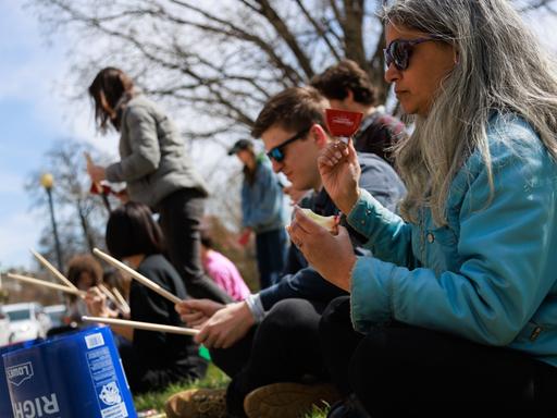 Klimaaktivisten sitzen bei einer Protestaktion auf dem Boden und trommeln auf Eimern.