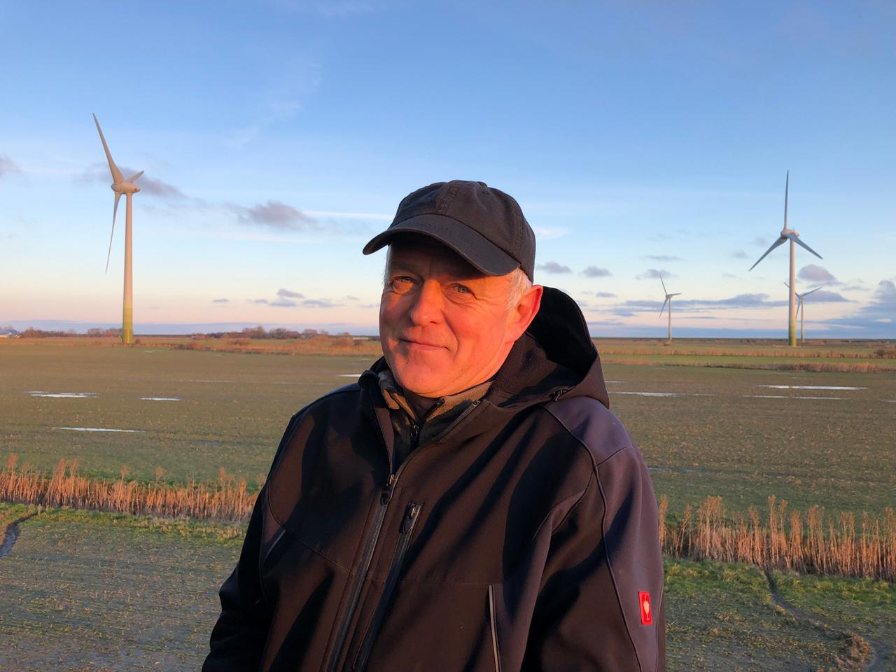 Kai Edlefsen steht mit Schirmmütze und dicker Jacke vor einem Feld, auf dem Windkraftanlagen stehen. Kai Edlefsen steht mit Schirmmütze und dicker Jacke vor einem Feld, auf dem Windkraftanlagen stehen.
