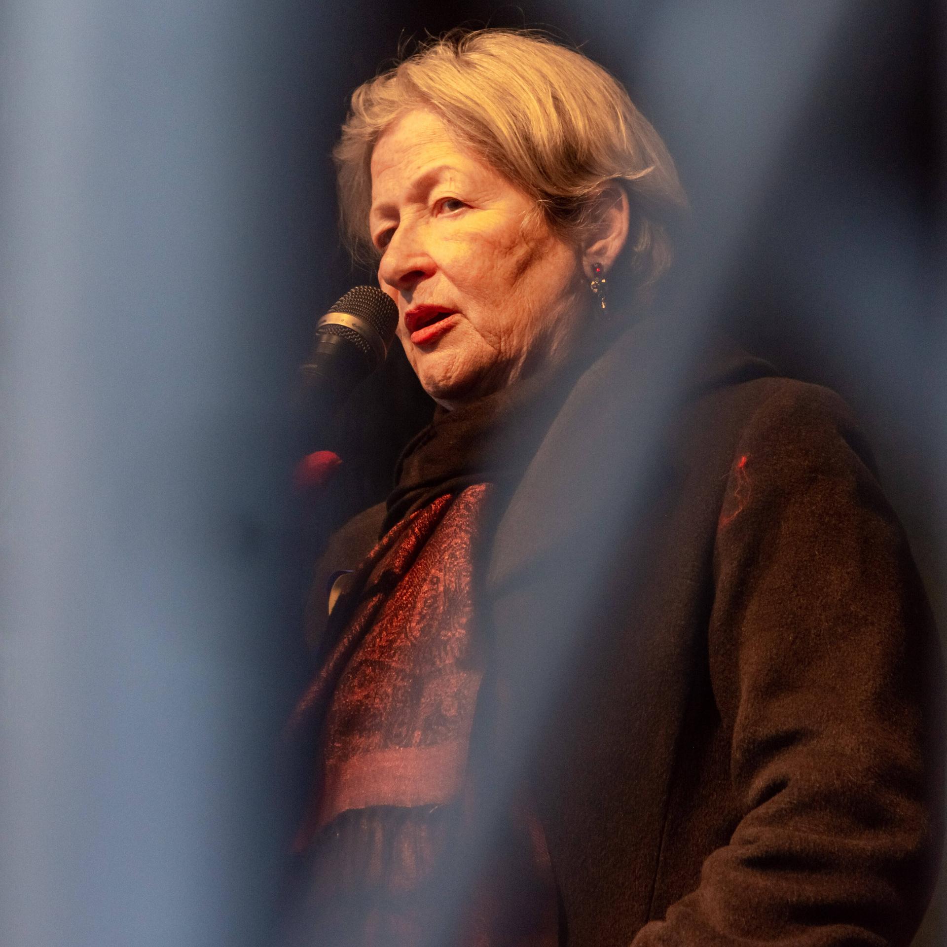 Die österreichische Schriftstellerin Susanne Scholl spricht bei einer Demonstration auf einer Bühne in ein Mikrofon 
