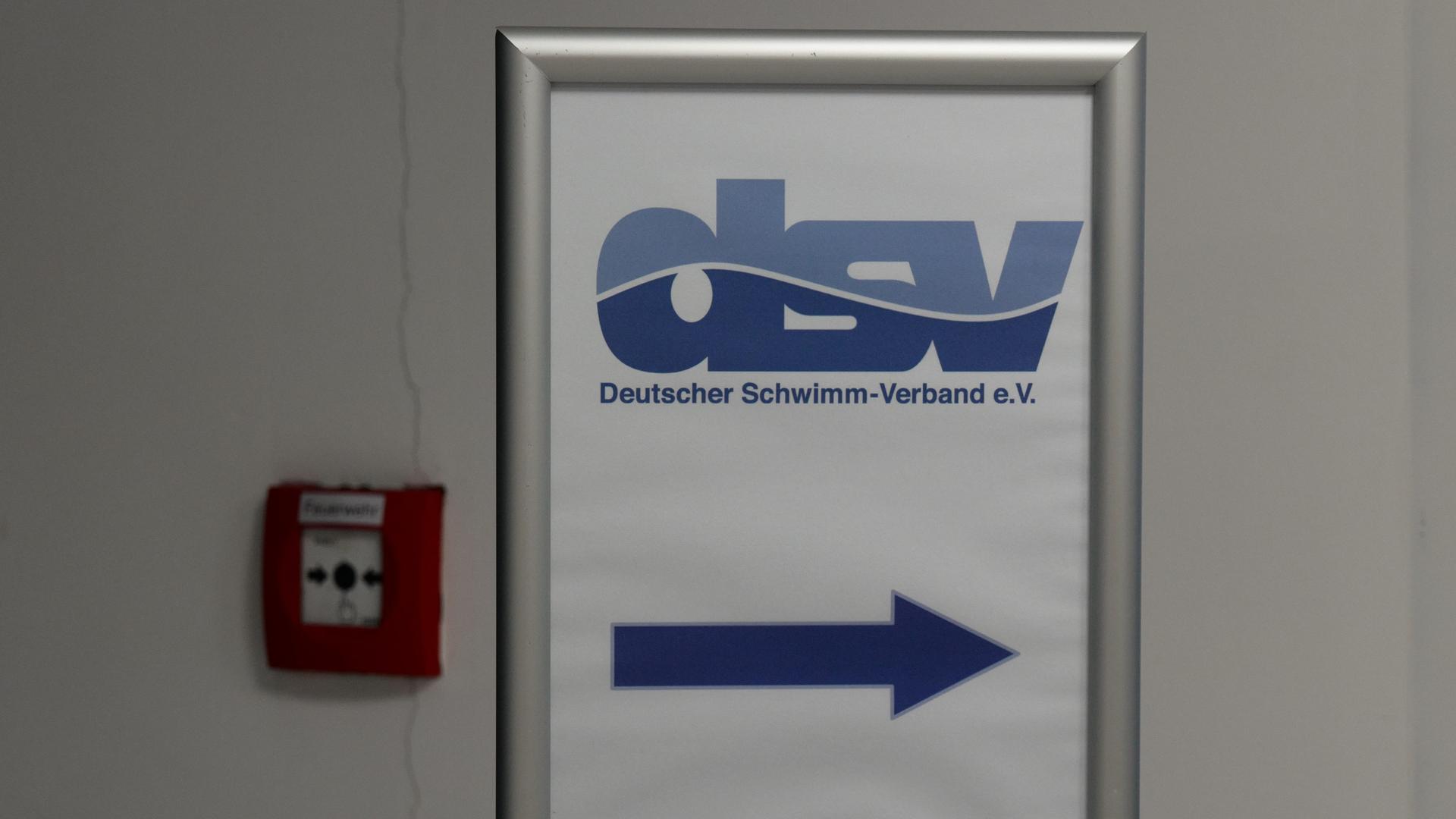 Auf dem Schild mit blauer Schrift auf weißem Grund zeigt ein pfeil nach rechts. Es hängt an einer Wand neben einem Feuer-Notmeldeknopf. Auf dem Schild mit blauer Schrift auf weißem Grund zeigt ein pfeil nach rechts. Es hängt an einer Wand neben einem Feuer-Notmeldeknopf.