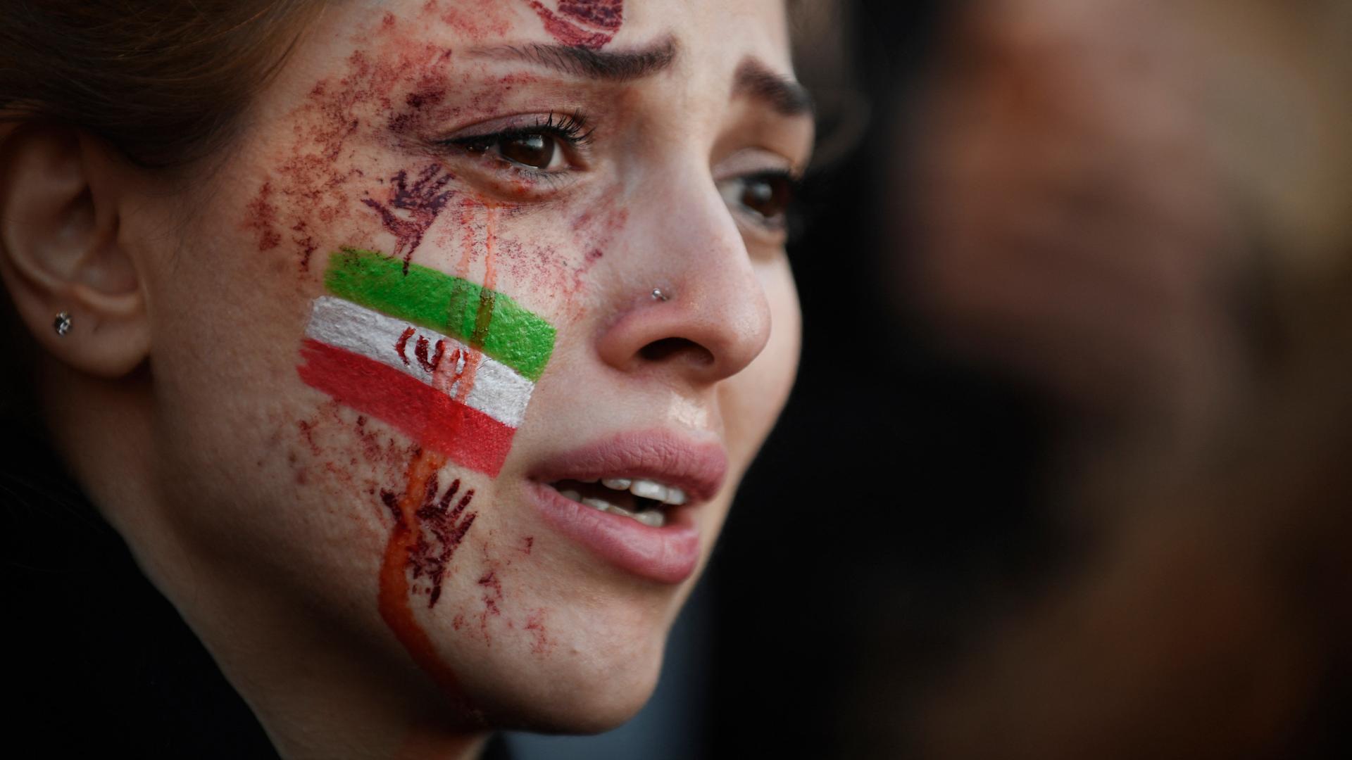 Eine junge Frau mit der von Tränen verschmierten iranischen Flagge und roten Händen auf ihrem Gesicht. Auf einer Demonstration wegen des Todes von Mahsa Amini im Iran. Paris, 9.Oktober 2022. 