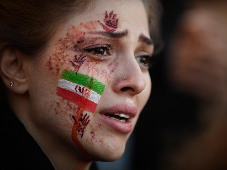 Eine junge Frau mit der von Tränen verschmierten iranischen Flagge und roten Händen auf ihrem Gesicht. Auf einer Demonstration wegen des Todes von Mahsa Amini im Iran. Paris, 9.Oktober 2022. 