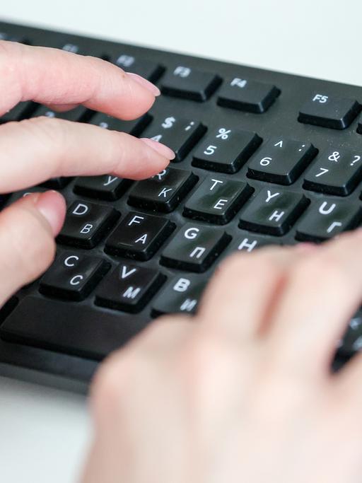 Hände tippen auf einer Computertastatur mit kyrillischen Buchstaben.