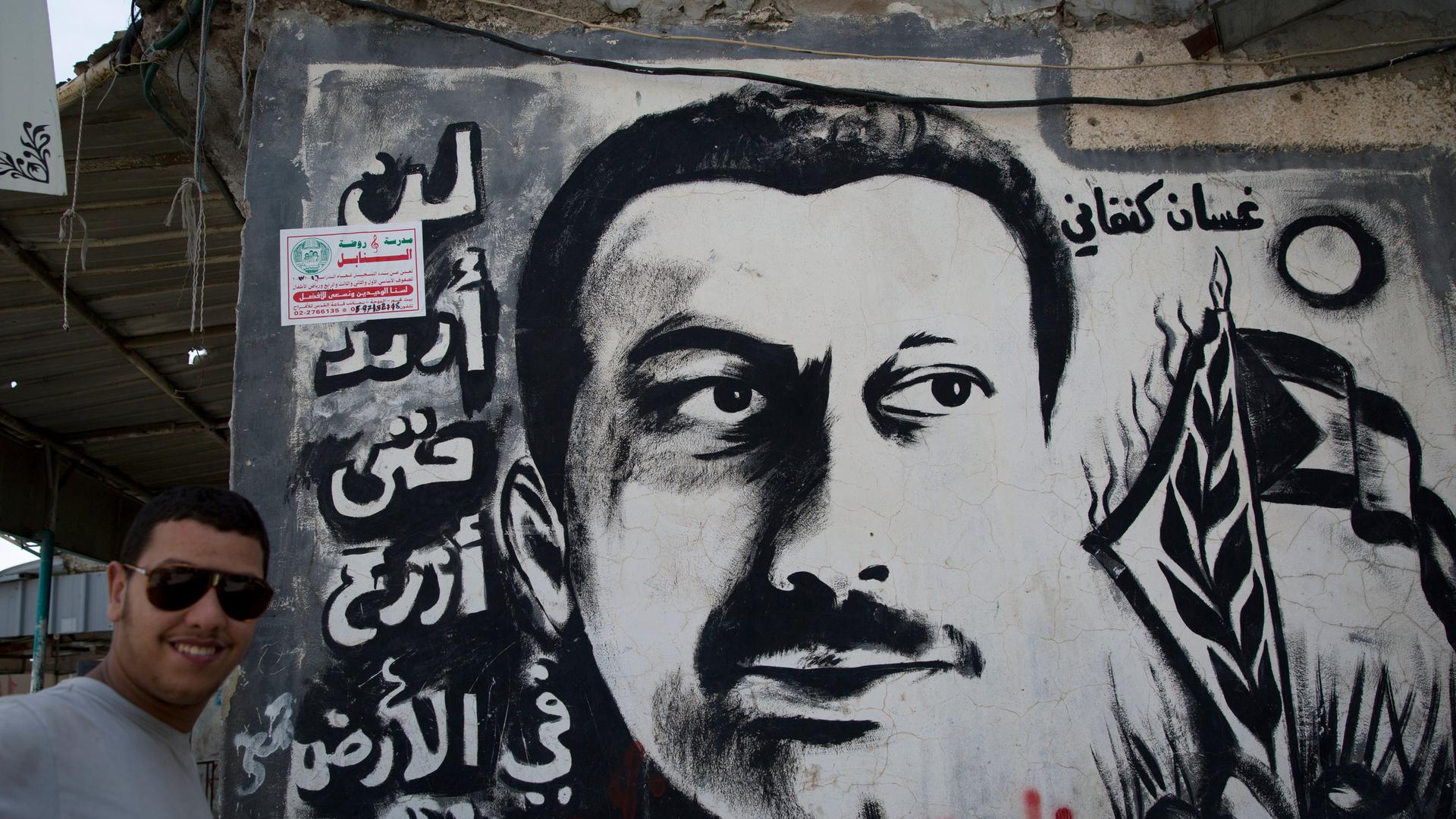 Ein palästinensischer Flüchtling steht neben einem Graffito, das den palästinensischen Schriftsteller Ghassan Kanafani zeigt mit der Aufschrift, "Ich werde nicht aufgeben, bevor ich mein Paradies auf Erden errichtet habe" Ein palästinensischer Flüchtling steht neben einem Graffito, das den palästinensischen Schriftsteller Ghassan Kanafani zeigt mit der Aufschrift, "Ich werde nicht aufgeben, bevor ich mein Paradies auf Erden errichtet habe"