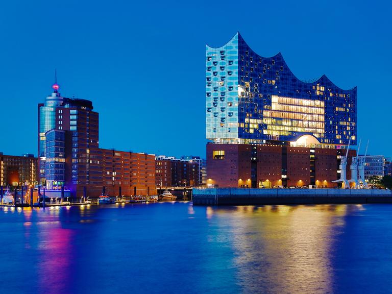 Ein blauer, wolkenloser Himmel wie man ihn abends beobachten kann, wenn die Sonne schon tief gesunken ist, aber der Himmel trotzdem noch eine restliche Helligkeit hat. Das Panorama zeigt die Umrisse der Elbphilharmonie in Hamburg.