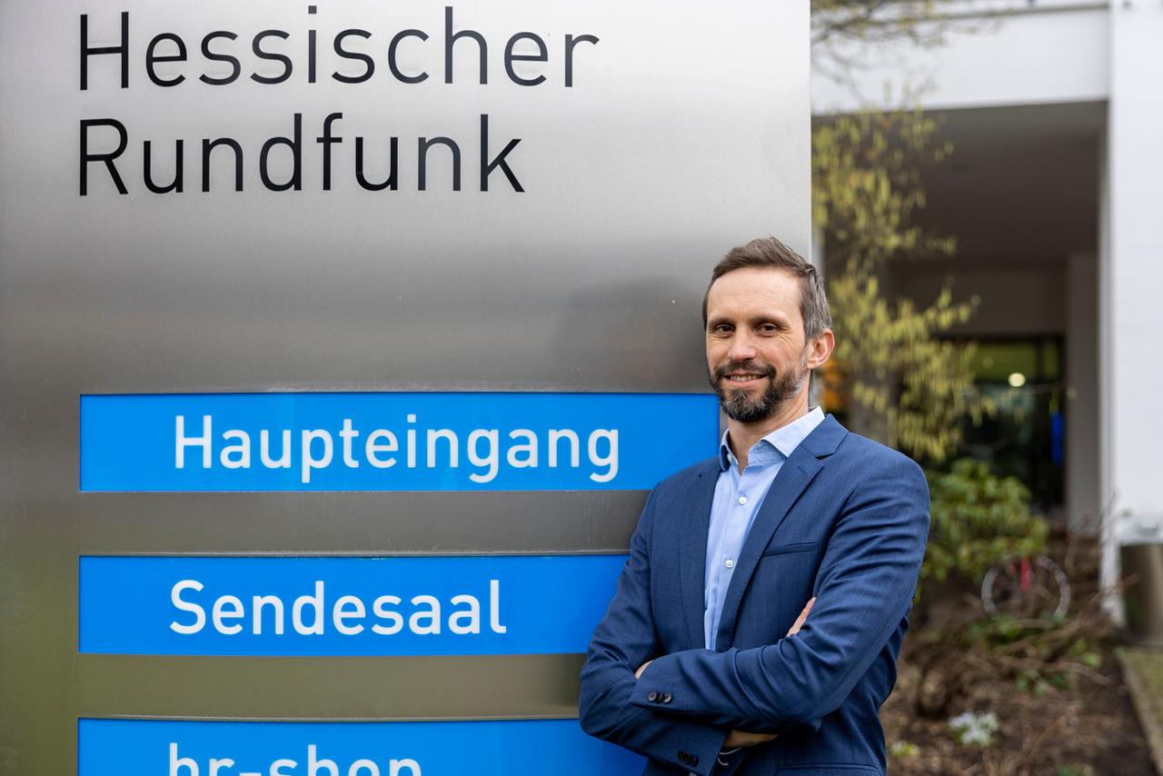Florian Hager, Intendant, steht vor dem HR-Rundfunkhaus in der Bertramstrasse. Neben ihm die Schilder "Haupteingang" und "Sendesaal".