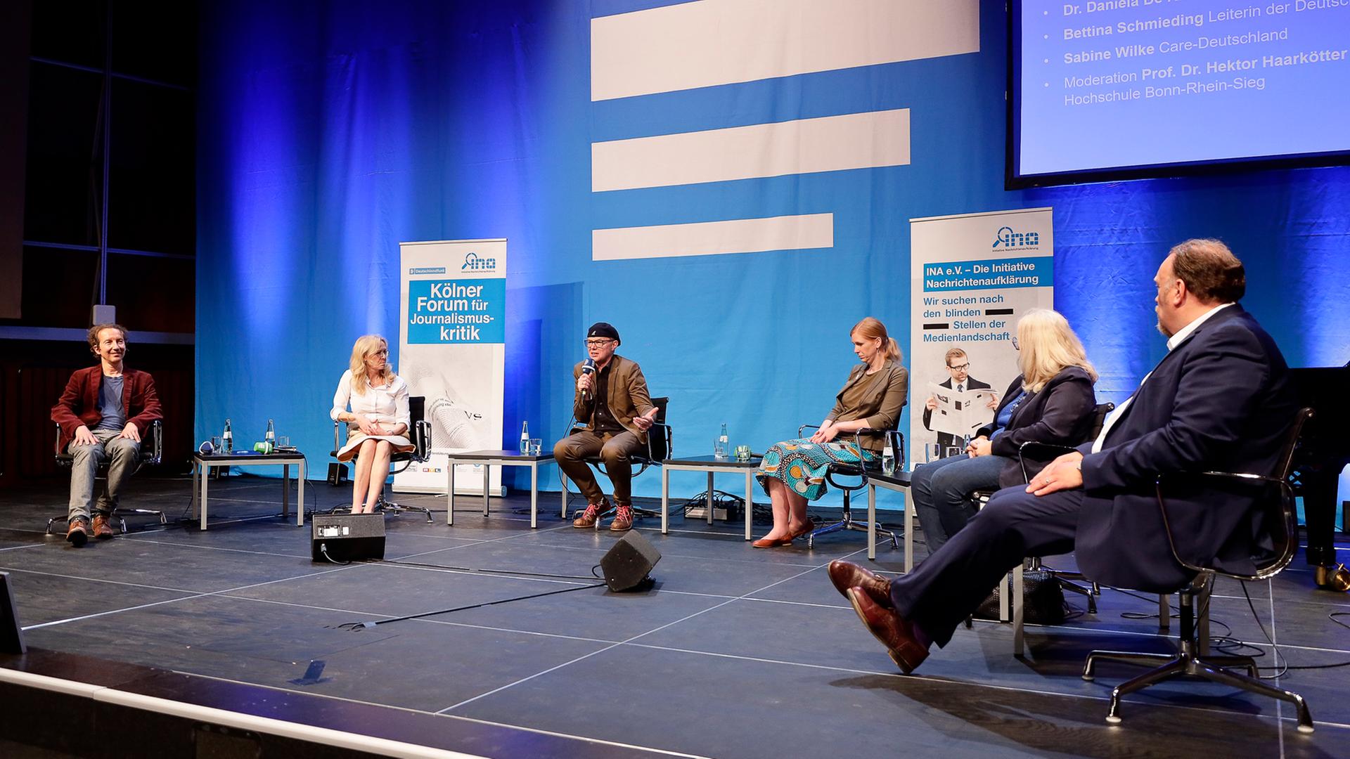 Die Gäste und der Moderator des Panels sitzen auf der Bühne vor einem großen Deutschlandfunk-Logo. Die Gäste und der Moderator des Panels sitzen auf der Bühne vor einem großen Deutschlandfunk-Logo.