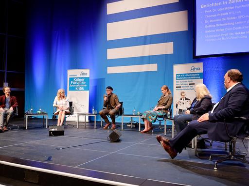 Die Gäste und der Moderator des Panels sitzen auf der Bühne vor einem großen Deutschlandfunk-Logo.