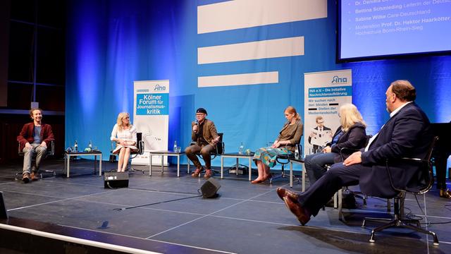 Die Gäste und der Moderator des Panels sitzen auf der Bühne vor einem großen Deutschlandfunk-Logo.