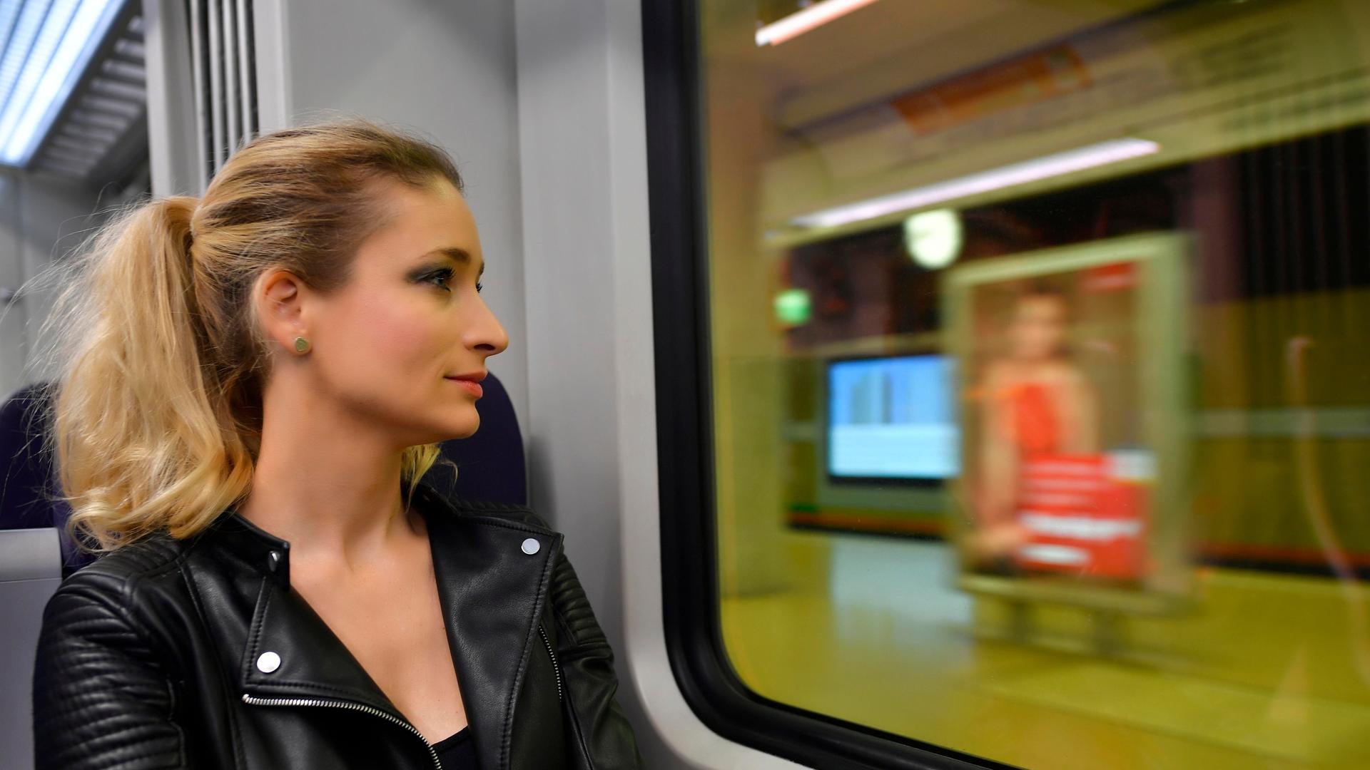 Eine Frau ohne Mundschutzmaske sitzt in Zug und schaut aus dem Fenster 