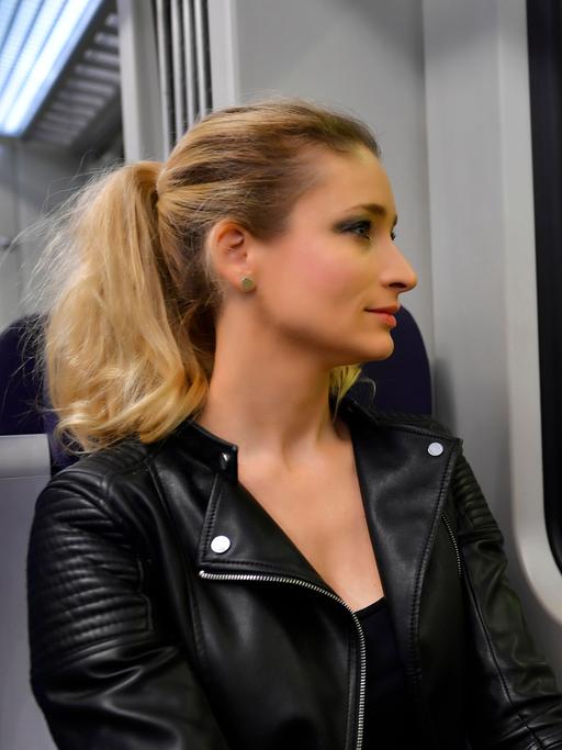 Eine Frau ohne Mundschutzmaske sitzt in Zug und schaut aus dem Fenster 