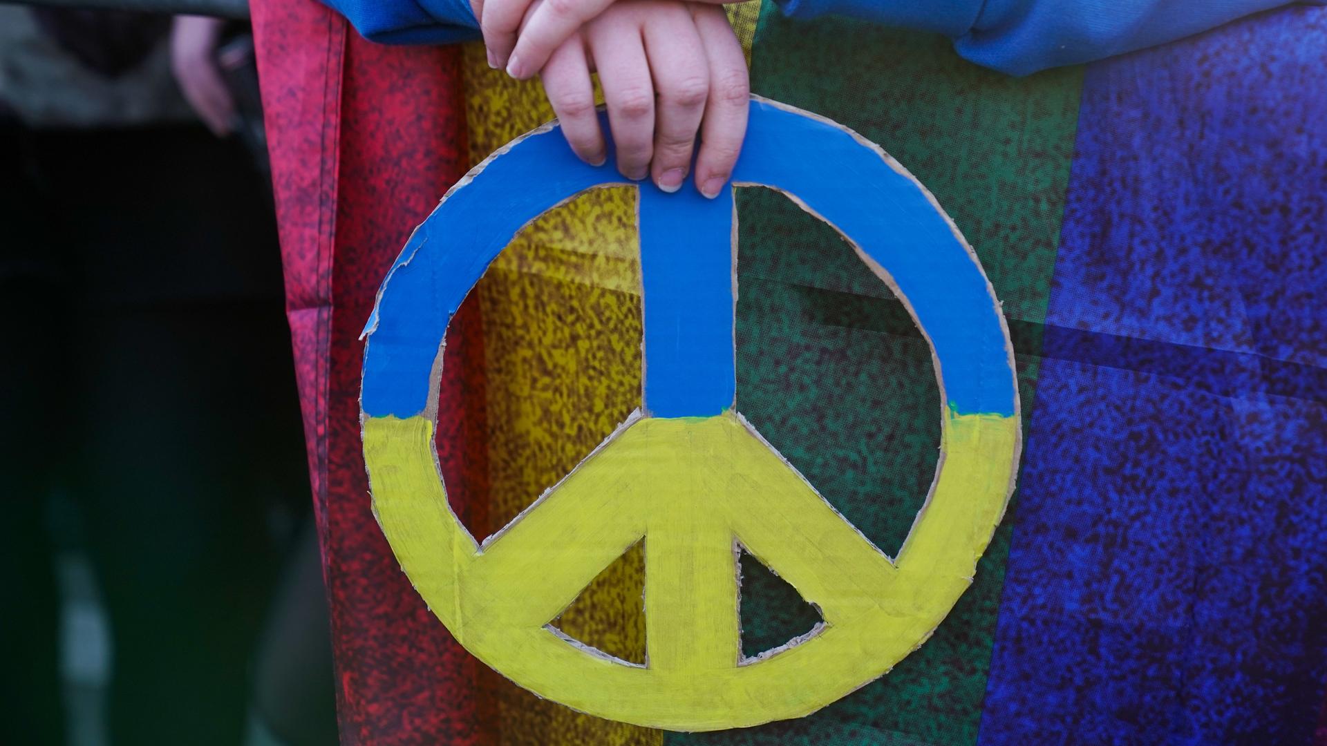 Zwei Hände halten das Symbol für Frieden in den ukrainischen Nationalfarben Blau und Gelb. Es handelt sich um eine Teilnehmende an einer Friedenskundgebung in Berlin anlässlich des Krieges in der Ukraine. Zwei Hände halten das Symbol für Frieden in den ukrainischen Nationalfarben Blau und Gelb. Es handelt sich um eine Teilnehmende an einer Friedenskundgebung in Berlin anlässlich des Krieges in der Ukraine.