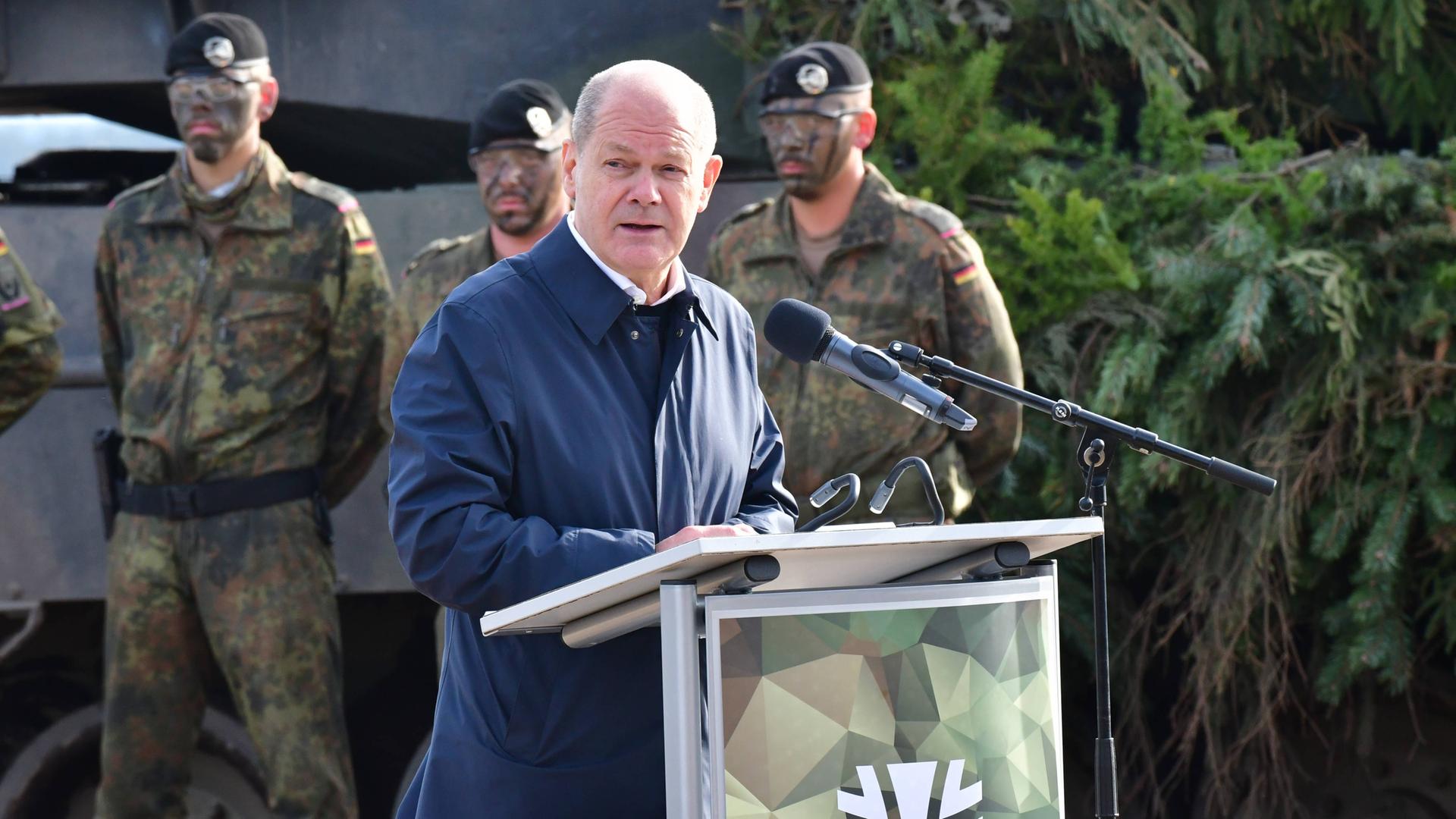 Bundeskanzler Olaf Scholz steht an einem Rednerpult vor Bundeswehrsoldaten, im Hintergrund ein Leopard-Kampfpanzer. 
