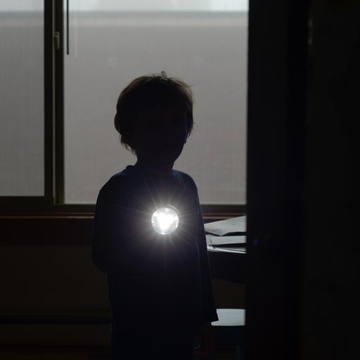 Ein junger Mensch steht mit einer Taschenlampe im Dunkeln und leuchtet in Richtung der Betrachtenden. Zu sehen sind nur Umrisse.