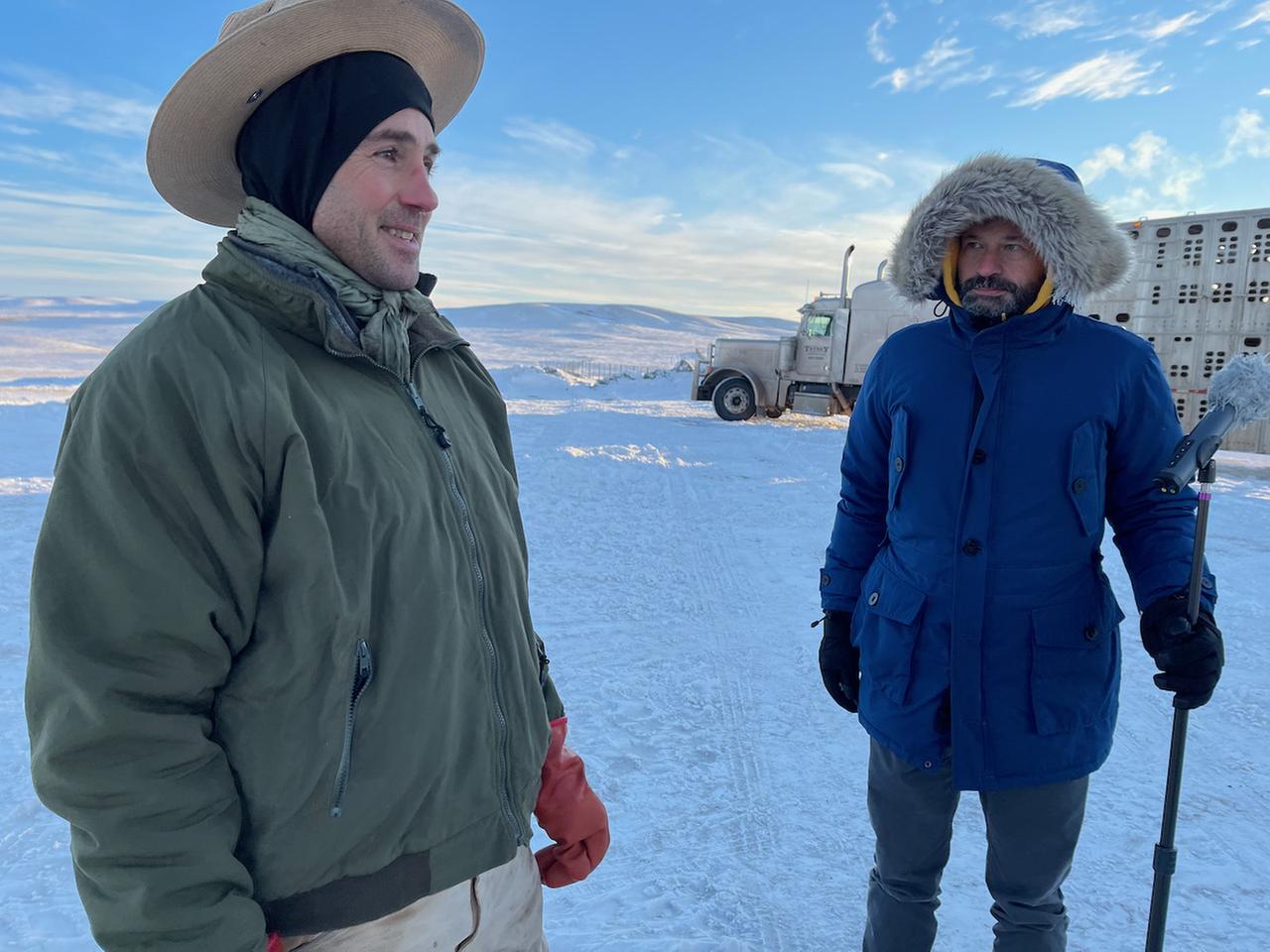 Zwei Männer mit dicken Anoraks, Mützen und Handschuhen stehen unter blauem Himmel in einer Schneelandschaft. Zwei Männer mit dicken Anoraks, Mützen und Handschuhen stehen unter blauem Himmel in einer Schneelandschaft.
