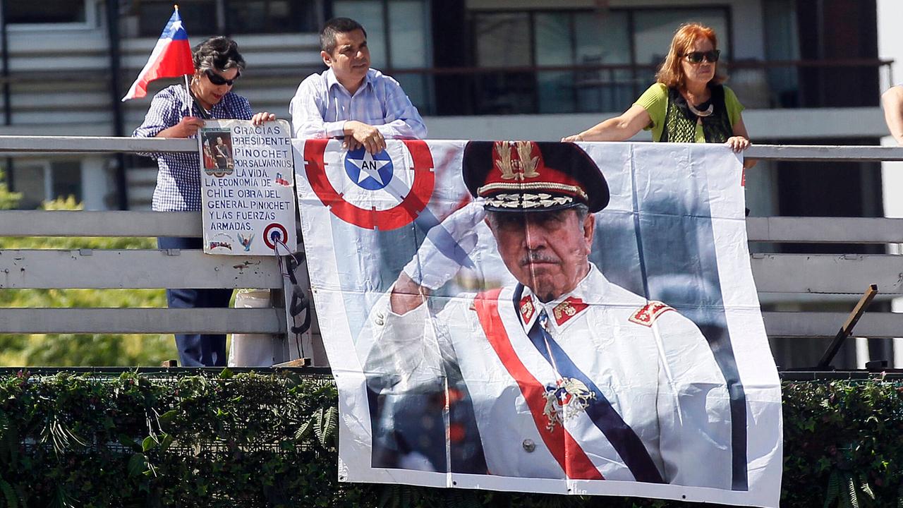 Zwei Personen hängen ein großes Plakat mit dem Bild von Augusto Pinochet ein Geländer hinrunter.