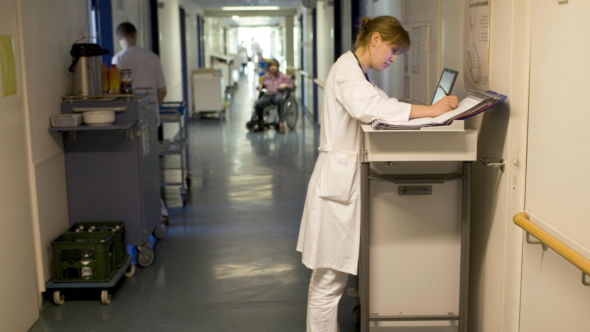 Blick in einen Krankenhausflur, in dem eine Ärztin etwas in ihren Unterlagen notiert. Blick in einen Krankenhausflur, in dem eine Ärztin etwas in ihren Unterlagen notiert.