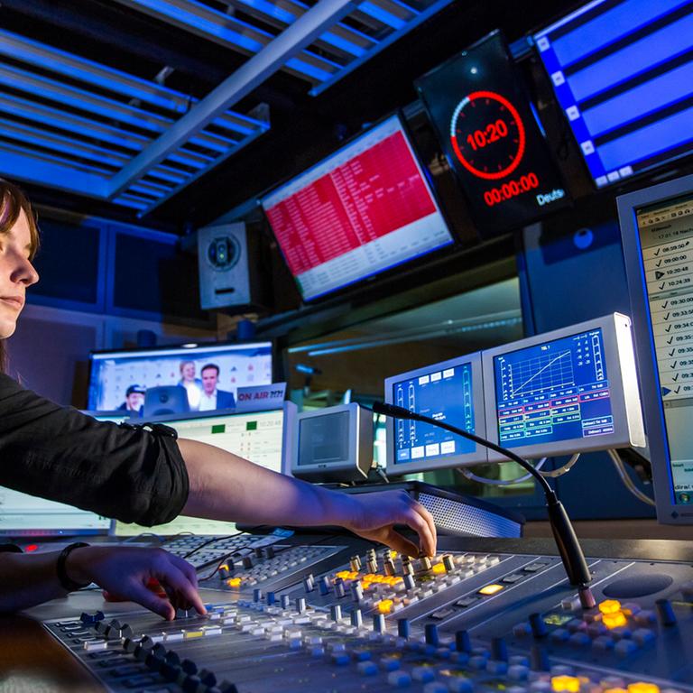 Eine junge Frau sitzt in einem Aufnahmestudio vor Monitoren und bedient Reglerknöpfe