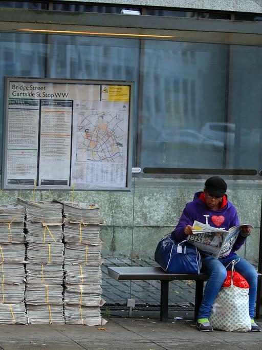 Eine Frau blättert in einer Zeitung, während sie in Manchester auf den Bus wartet.