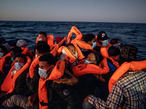 Menschen mit Masken und orangenen Schwimmwesten dicht gedrängt auf einem Boot