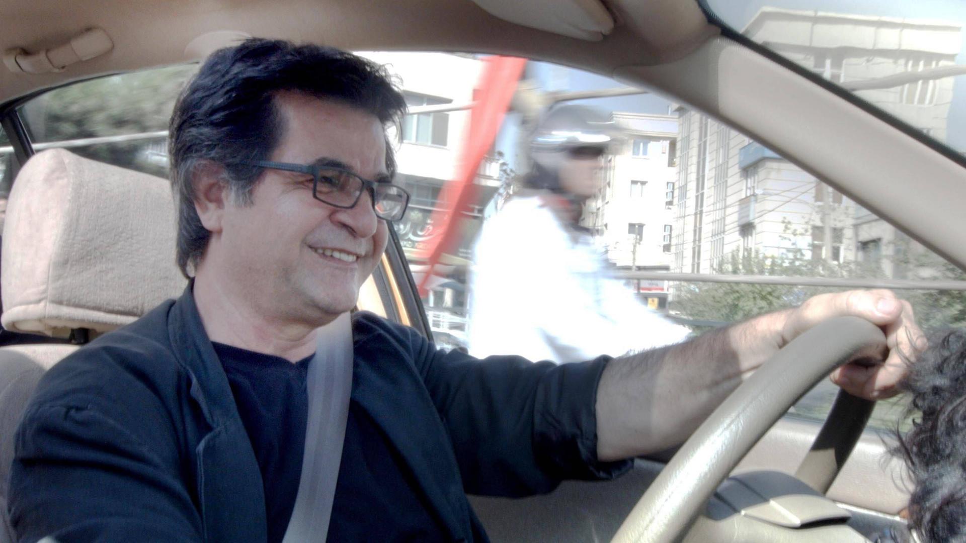 Jafar Panahi sitzt in einem Auto am Steuer und lächelt. Jafar Panahi sitzt in einem Auto am Steuer und lächelt.