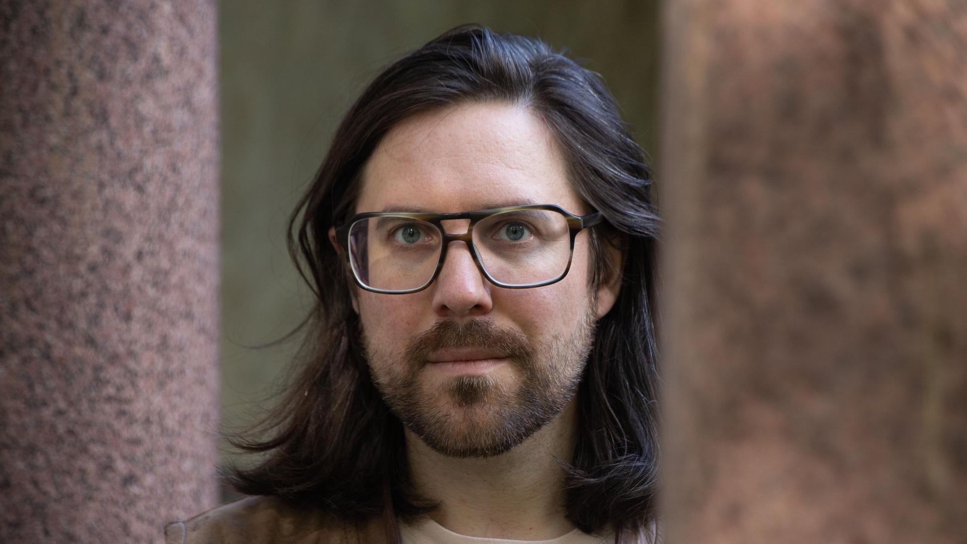 Tillmann Severin, ein Mann mit schulterlangen Haaren und Brille, blickt in die Kamera. Tillmann Severin, ein Mann mit schulterlangen Haaren und Brille, blickt in die Kamera.