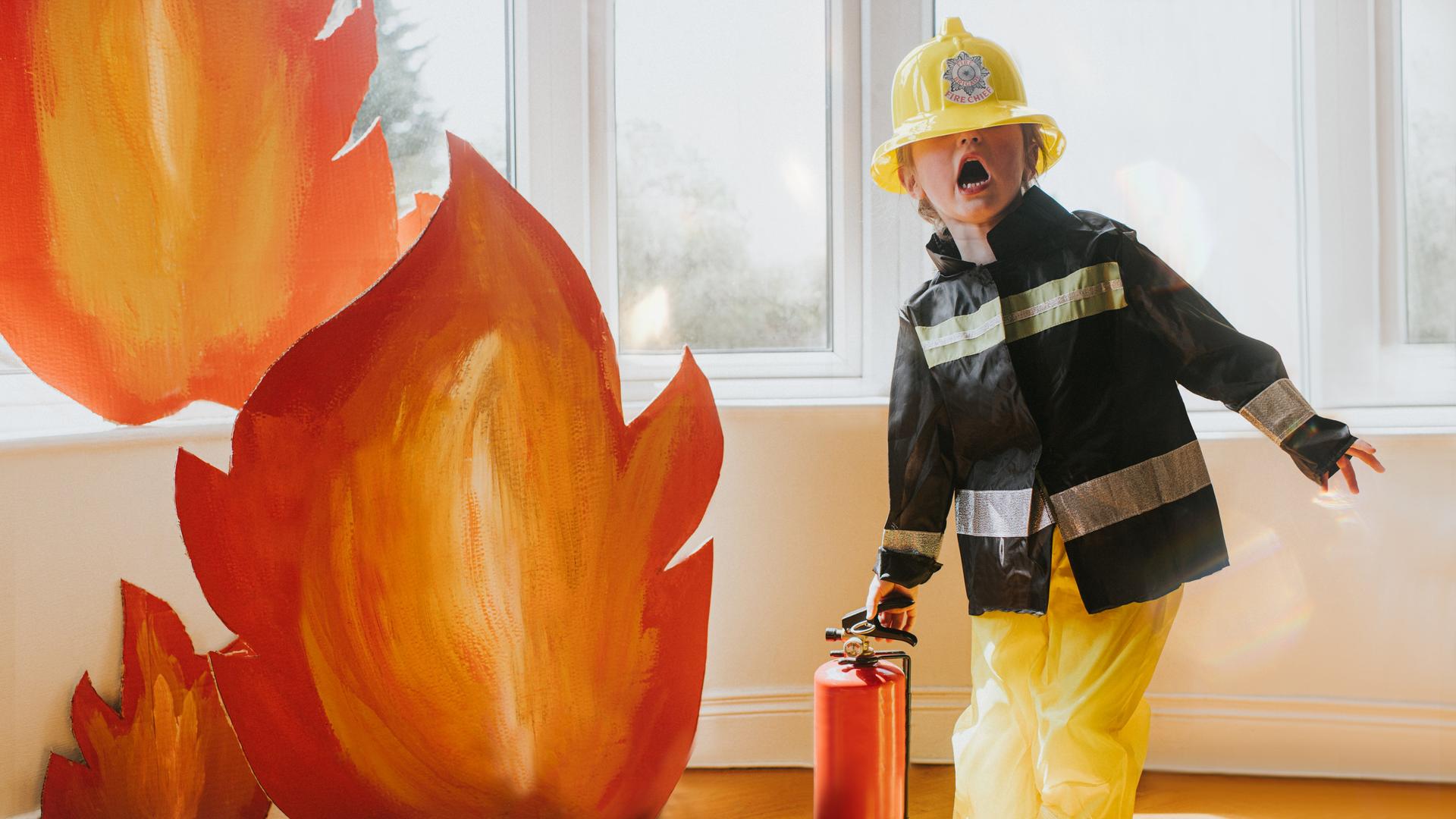 Ein Kind verkleidet als Feuerwehr, mit Helm, Anzug, Feuerlöscher und Flammen aus Pappe. Ein Kind verkleidet als Feuerwehr, mit Helm, Anzug, Feuerlöscher und Flammen aus Pappe.