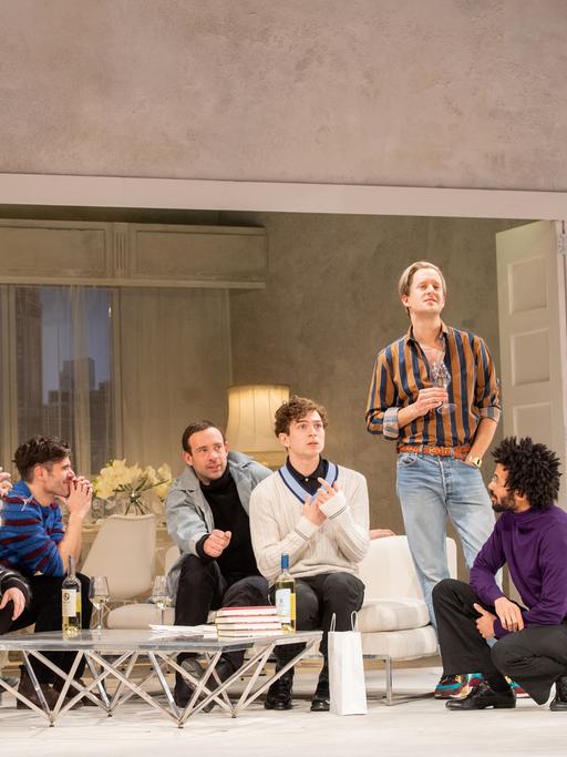 Foto von der Inszenierung: Sieben junge Männer unterhalten sich angeregt auf einer Couch-Landschaft miteinander.