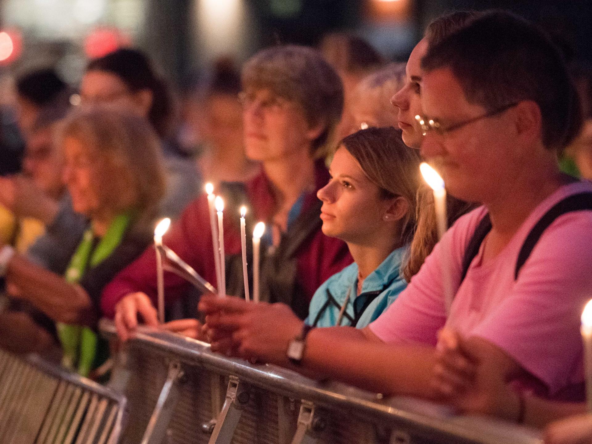 Viele Menschen halten Kerzen in der Hand und blicken konzentriert nach links aus dem Bild heraus.