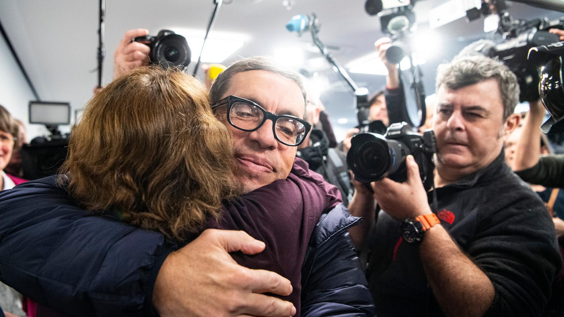 Jens Söring wird nach seiner Ankunft am Flughafen von einer Unterstützerin umarmt. Nach mehr als drei Jahrzehnten in Haft trifft der Diplomatensohn Jens Söring 2019 am Flughafen ein. Jens Söring wird nach seiner Ankunft am Flughafen von einer Unterstützerin umarmt. Nach mehr als drei Jahrzehnten in Haft trifft der Diplomatensohn Jens Söring 2019 am Flughafen ein.