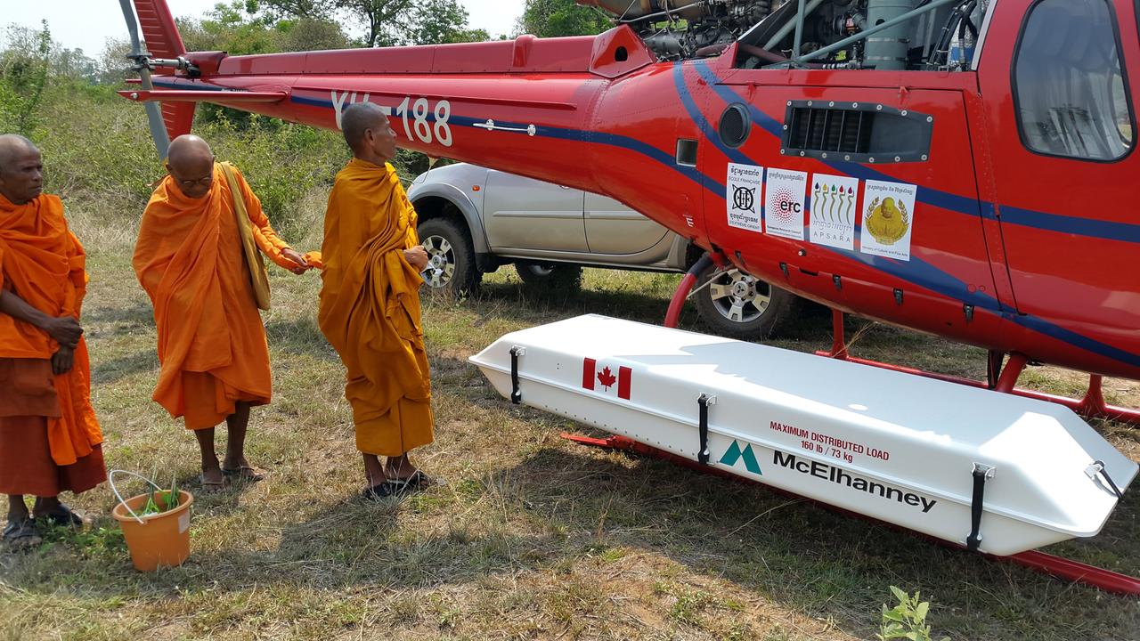Buddhistische Mönche stehen neben einem Hubschrauber mit dem LiDAR-Instrument, Tempelkomplex Banteay Chhmar, Kambodscha Buddhistische Mönche stehen neben einem Hubschrauber mit dem LiDAR-Instrument, Tempelkomplex Banteay Chhmar, Kambodscha