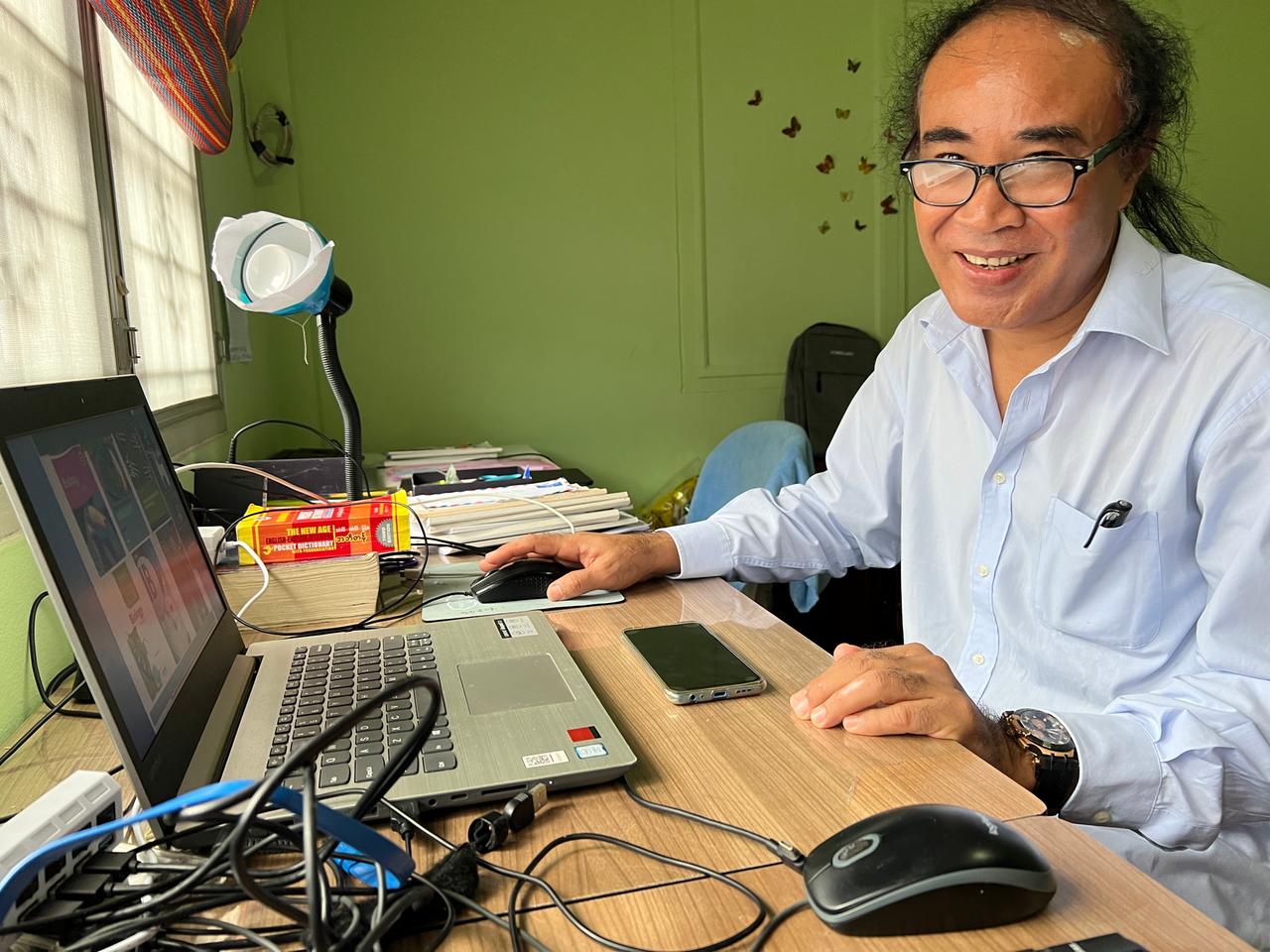 Ein Mann mit Brille und hellblauem Hemd sitzt an einem Schreibtisch, auf dem ein Laptop steht. Ein Mann mit Brille und hellblauem Hemd sitzt an einem Schreibtisch, auf dem ein Laptop steht.