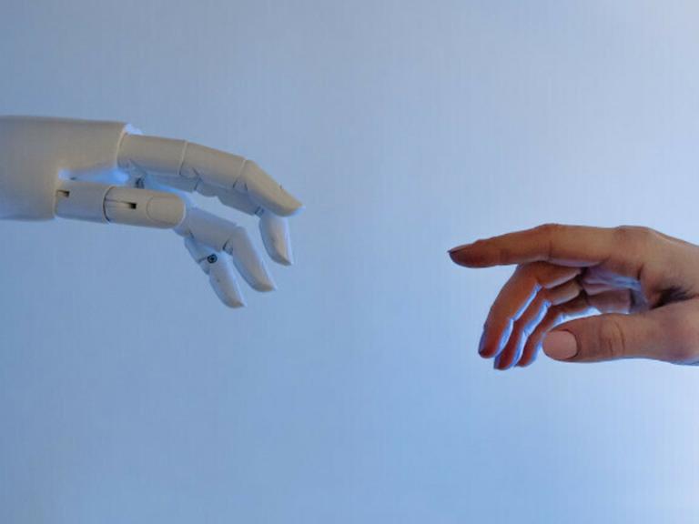 Die Hand eines Roboters und eine menschliche Hand berühren sich fast.