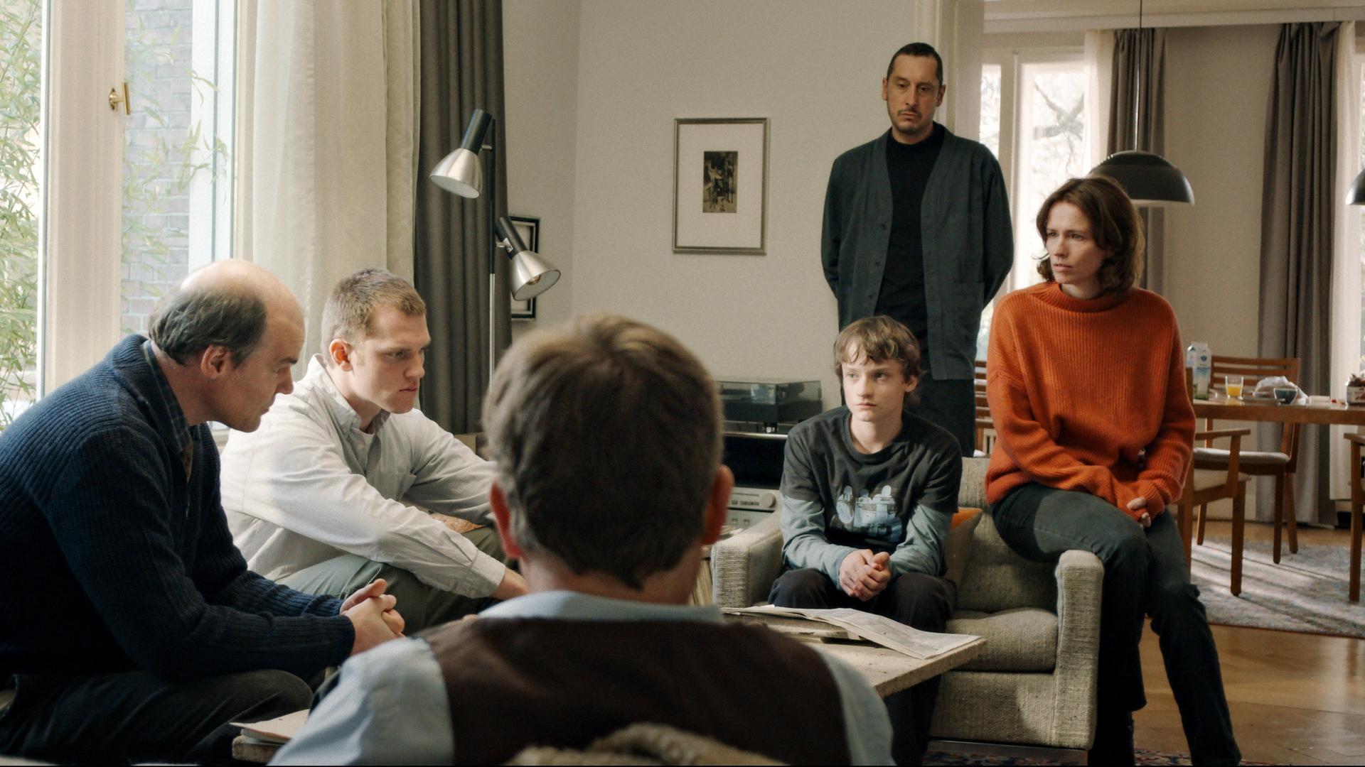 An einem Wohnzimmertisch sitzen Familie und Polizeiermittler beisammen und besprechen die Lage. An einem Wohnzimmertisch sitzen Familie und Polizeiermittler beisammen und besprechen die Lage.