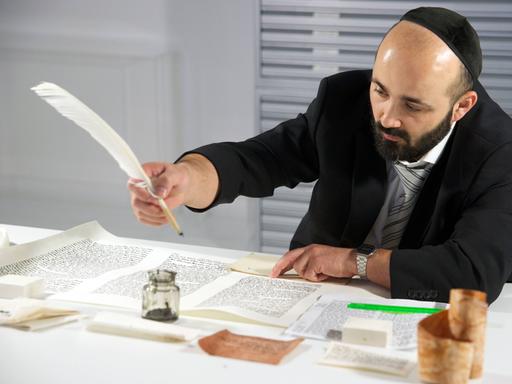 Der Rabbiner Reuven Yaacobov schreibt mit Feder und Tinte im Jüdischen Museum Berlin eine Torarolle.