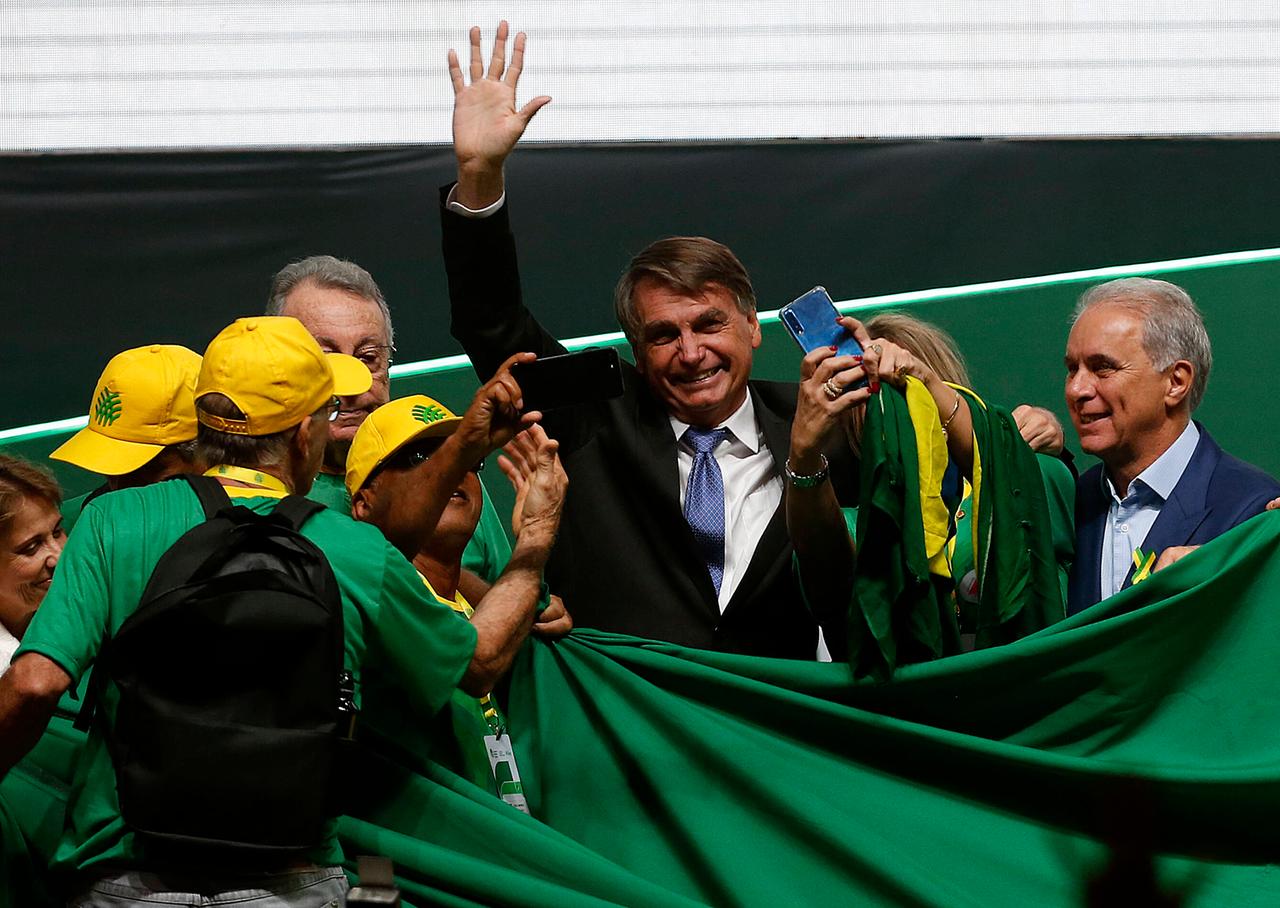 Bolsonaro steht in einer kleinen Schar von Anhängern mit gelben Käppis, überall sind grüne Laken und er winkt ins Publikum. Bolsonaro steht in einer kleinen Schar von Anhängern mit gelben Käppis, überall sind grüne Laken und er winkt ins Publikum.