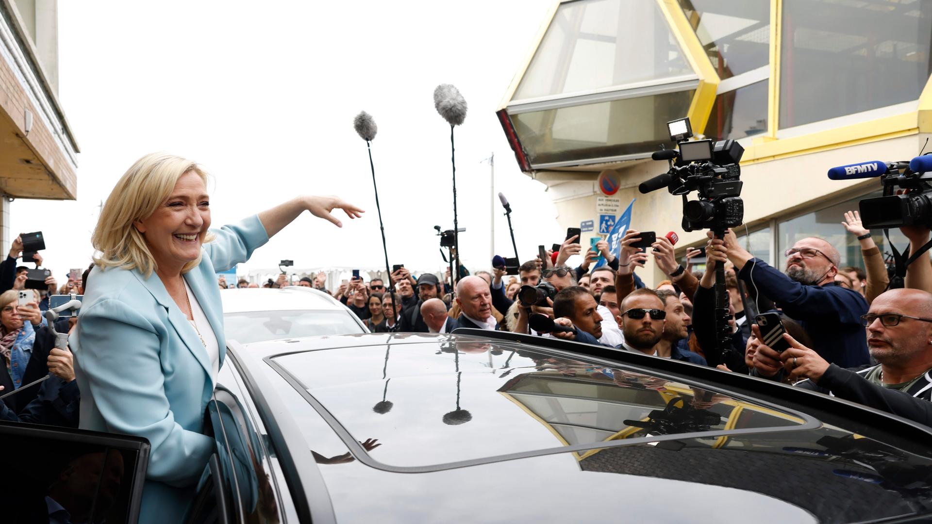 Marine Le Pen steht lachend in einer Menschenmenge, umgeben auch von zahlreichen Journalisten