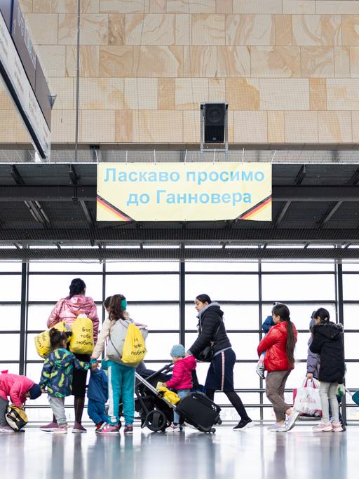 Ukrainische Geflüchtete laufen von rechts nach links durch eine Bahnhofshalle.