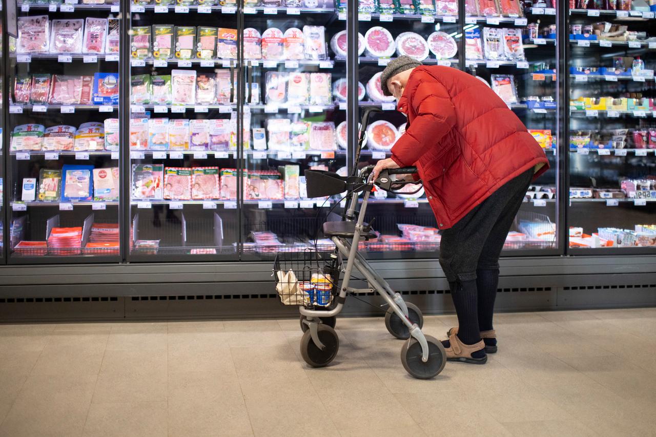 Eine Rentner mit Rollator steht vor einer Kühltheke im Supermarkt.