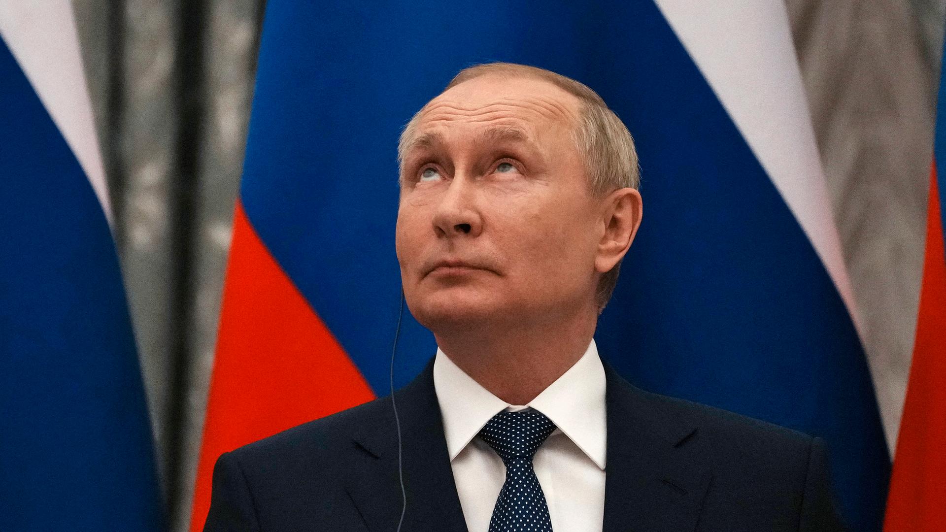 Wladimir Putin mit nach oben gerichteten Blick. Im Hintergrund ist die russiche Flagge zu sehen. Wladimir Putin mit nach oben gerichteten Blick. Im Hintergrund ist die russiche Flagge zu sehen.