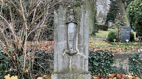 Ein alter Grabstein auf einem Friedhof. Darum Efeu und gefallenes Laub.