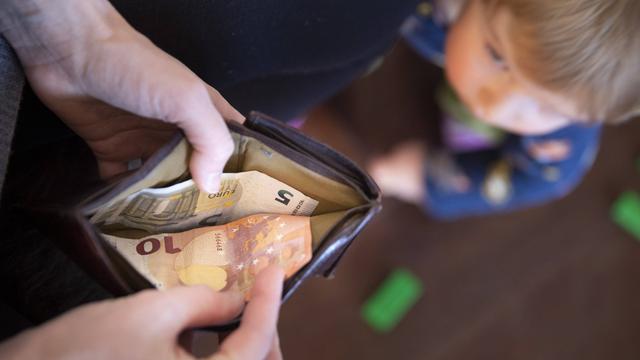 Blick von oben auf eine geöffnete Geldbörse und ein Kind, das auf diese schaut. In der Geldböse ist ein fünf und ein zehn Euro-Schein.