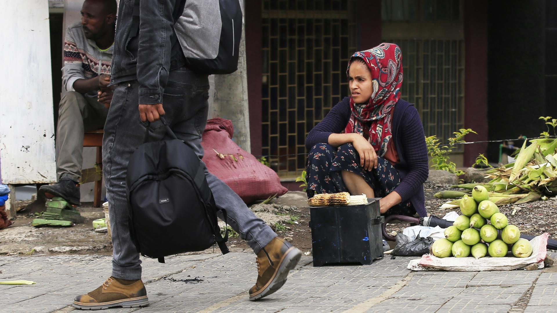Eine Straßenszene in Äthiopiens Haupststadt Addis Abeba: Eine Frau sitzt am Straßenrandd und verkauft Früchte. Ein männlicher Passant eilt vorbei. 