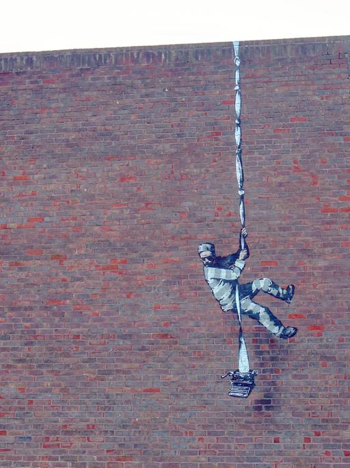 Banksys Wandbild an der Gefängnismauer von Reading zeigt einen Ausbrecher, der sich an zusammengeknoteten Schreibmaschinenseiten abseilt.