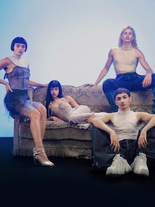 Studiofoto mit den ukrainischen und russischen Models Valeriia Karamann (links), Tanya Chudnovskaia (2. von links) Daniel Nikiforow (rechts oben) und Regisseur und Fotograf Mehran Djojan (rechts unten sitzend). Die jungen Leute sind stylisch frisiert und gekleidet.